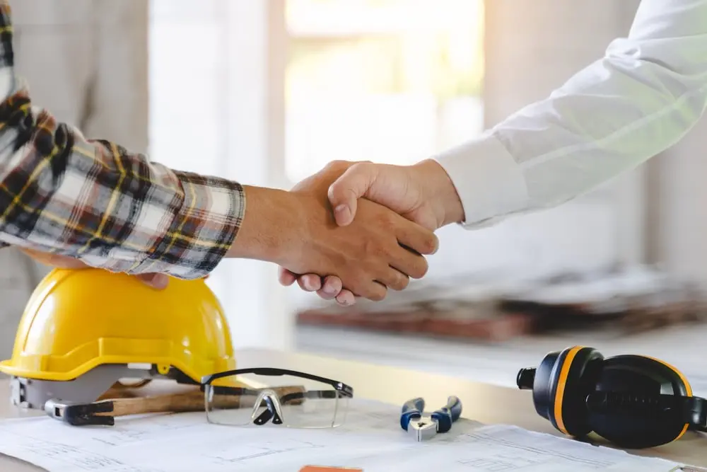 Handshake over construction plans and safety gear
